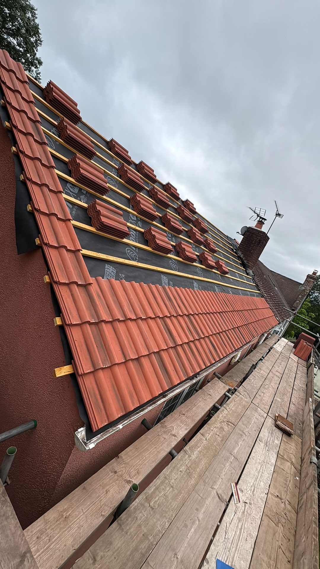 Red interlocking tiles being laid on new battens and membrane, re-roofing in progress, Glastonbury