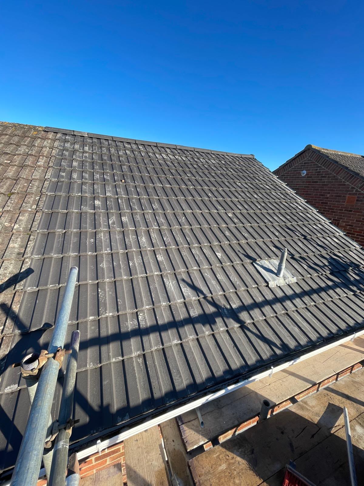 New dark grey interlocking tiles on a finished re-roof under a clear sky, Somerset