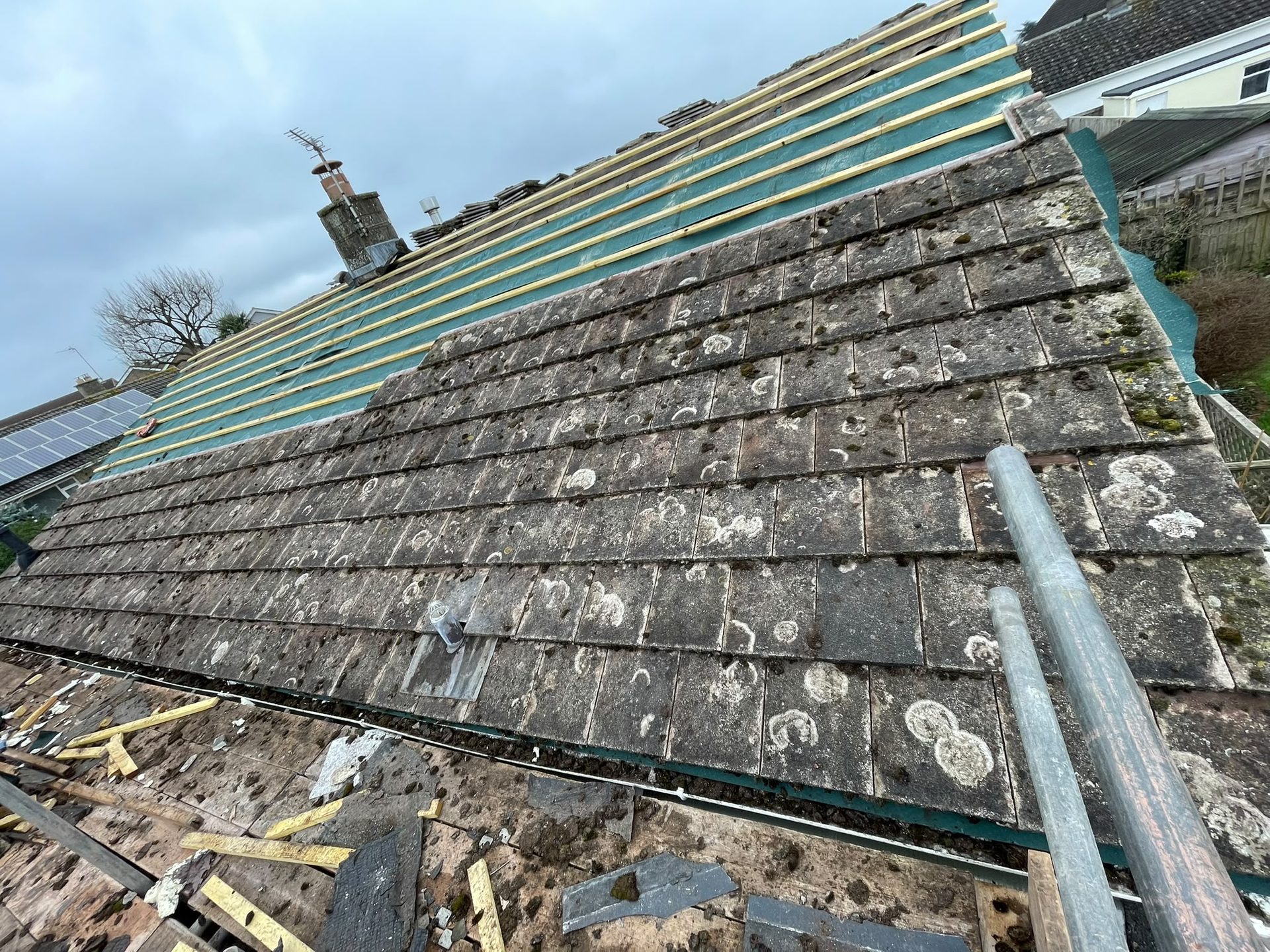 Old moss-covered concrete tiles being stripped with new membrane and battens fitted, re-roofing Somerset