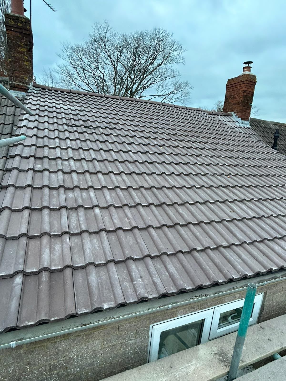 Completed brown interlocking tile re-roof between two brick chimneys, Somerset